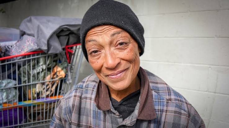 A woman smiling outdoors beside her belongings